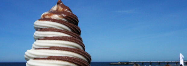 Schoko-Vanille-Eis (weiß und braun, gedreht, Softeis) vor dem blauen Meer.