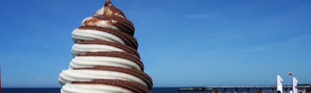 Eis und Meer. Foto: Kolberg-Cafe. Schoko-Vanille-Eis (weiß und braun, gedreht, Softeis) vor dem blauen Meer.