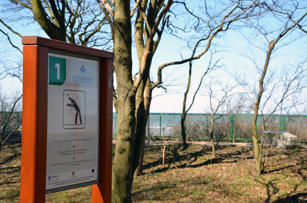 Fitnesscourse in Kolberg. Tafel, die die Übungen beschreibt, im Wald, im Hintergrund die Ostsee.Foto: Kolberg-Café