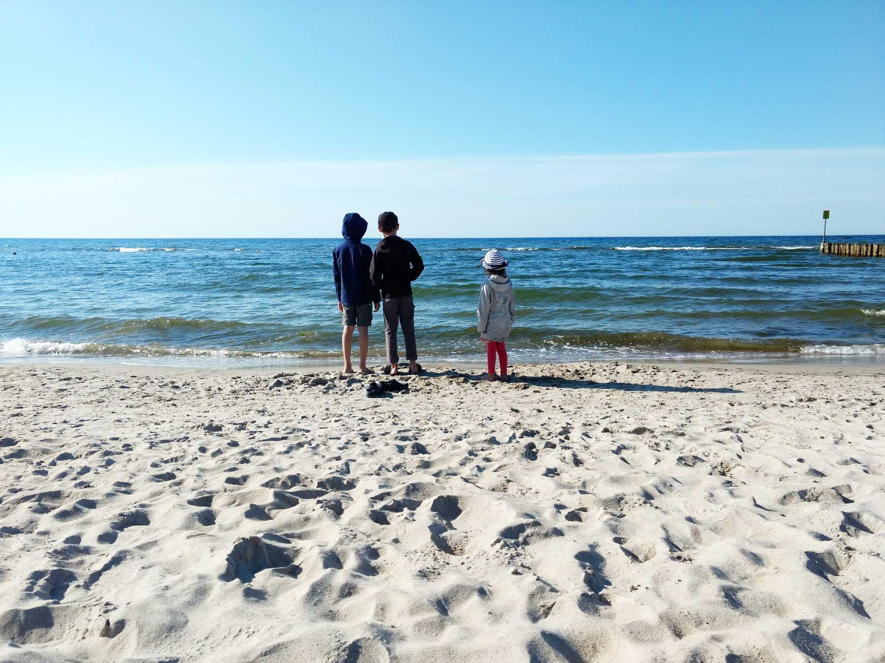 Kinder am Strand bei Kolberg, aufs Meer blickend bei blauem Himmel. Foto: Kolberg-Café